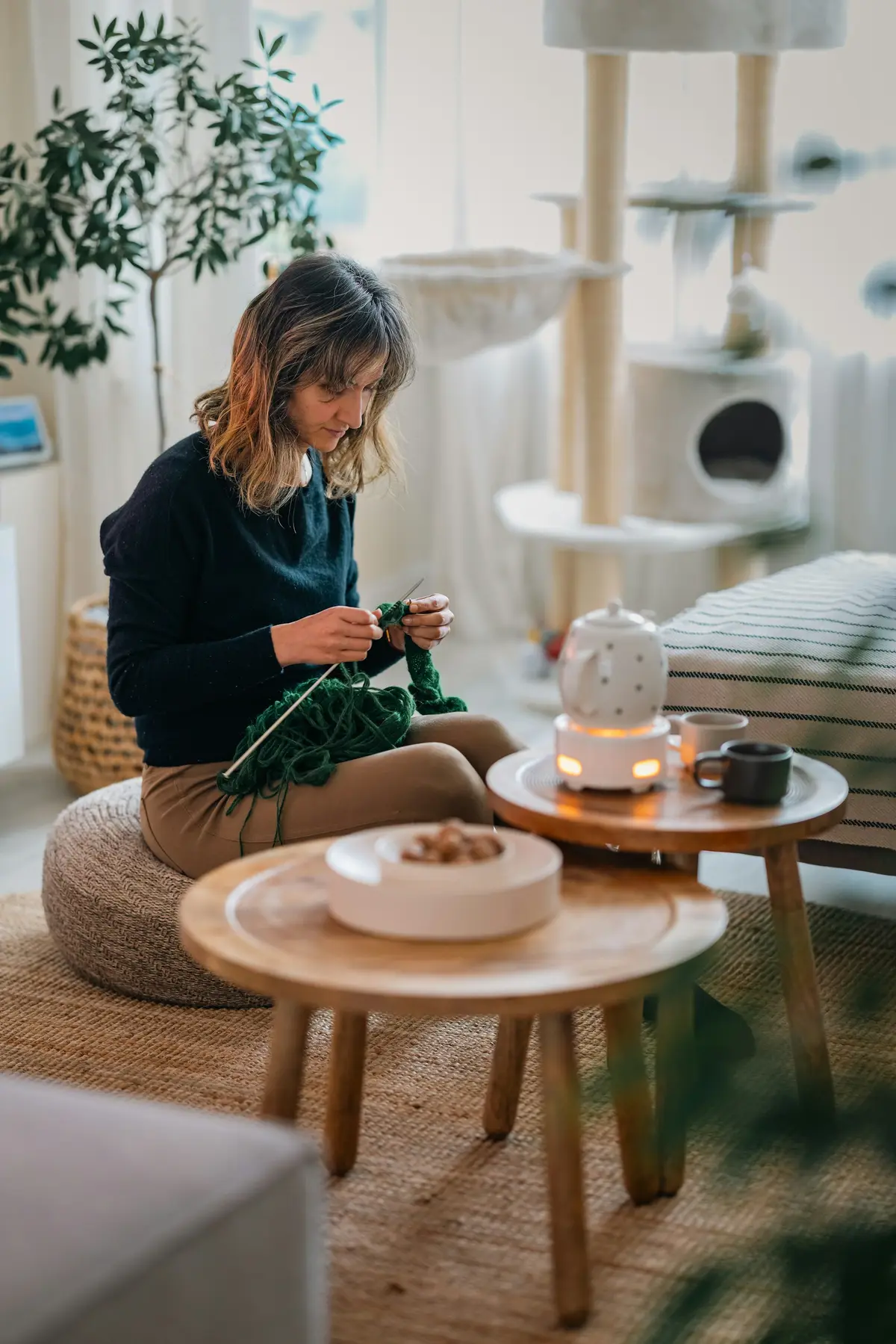 A woman knitting on a floor cushion in a bright, calm living room